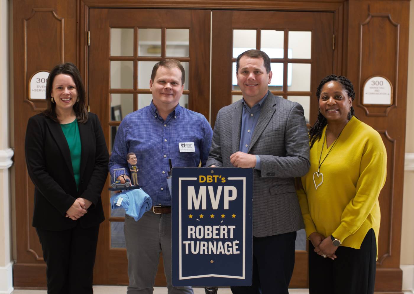 MC President Blake Thompson, second from right, presents the March DBT's MVP Award to Robert Turnage, director of web and creative communications, while Jenny Tate, left, vice president of marketing and communications, and Angela Riggs, assistant bursar and last month's DBT's MVP recipient, congratulate him.