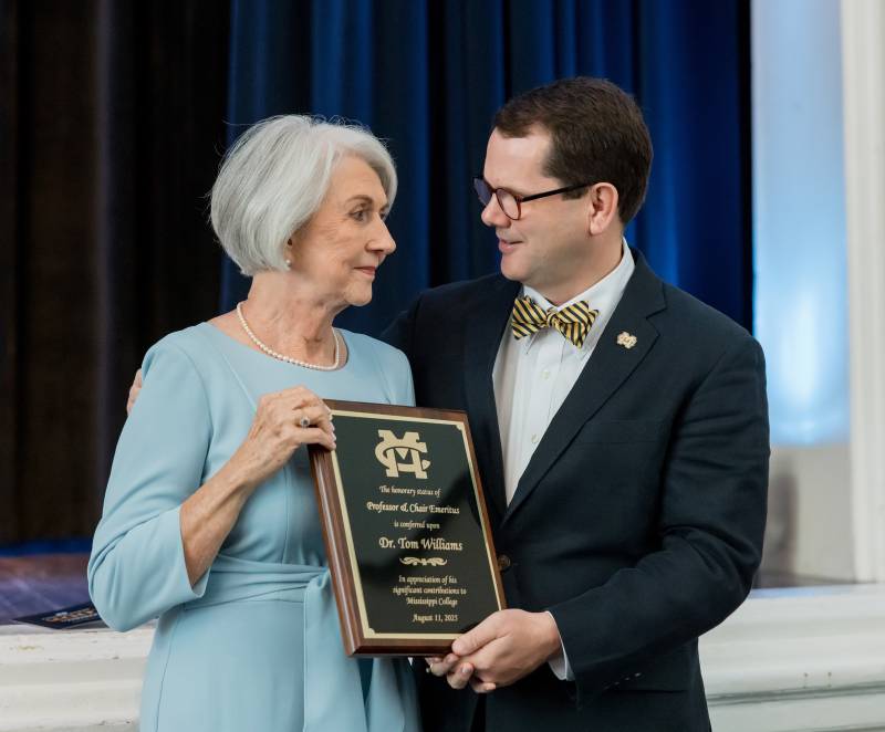 Mississippi College President Blake Thompson presents a plaque to Mary Williams, the widow of Tom Williams, conferring his new title as MC Professor Emeritus in the Department of Teacher Education and Leadership.