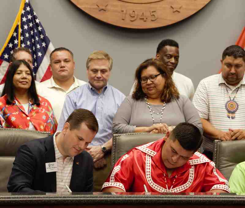 Surrounded by Choctaw Tribal Council members and Mississippi College leaders, Dr. Blake Thompson, front left, MC president, and Chief Cyrus Ben, front right, Mississippi Band of Choctaw Indians tribal chief, sign the memorandum of understanding between MC and the MBCI.