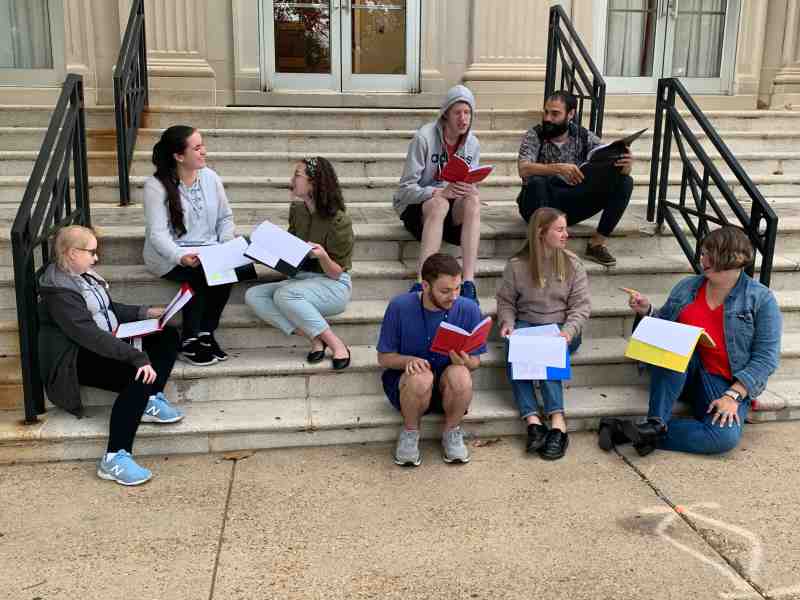MC performers rehearsing lines from “It’s a Wonderful Life: A Live Radio Play by Joe Landry” on the front steps of the Aven Fine Arts Building include, in front from left, Larkin Dorris, Carson Jones, Vanessa Sharp, Gordon Huey, Chloe Newton, and Abby Duggar, and in back from left, Jake Parker and David Baker.