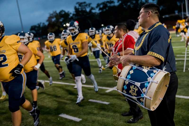 MBCI Tribal Chief Cyrus Ben, an MC alum, former football player, and 2022 Order of the Golden Arrow recipient, uses a drum to herald the arrival of the Mississippi College football team.