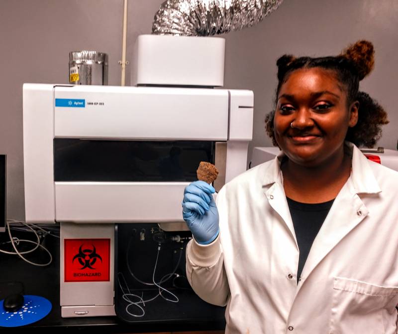 Takaye Farmer, a senior chemistry major from Memphis, holds a pottery shard that will be crushed, prepared, and fed into the state-of-the-art ICP-OES instrument for analysis.